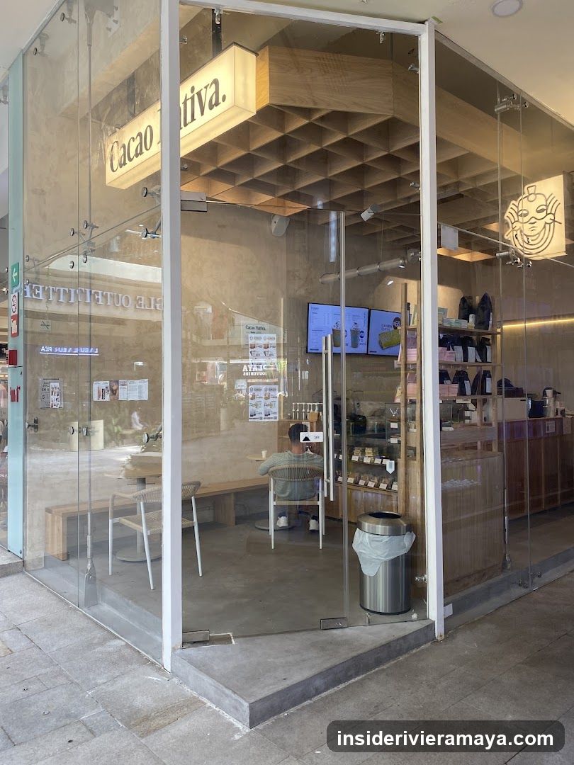 A glass-fronted corner storefront with a wooden ceiling grid and a lit sign reading 'Cacao Tiva'. Inside, a customer sits at a table, and digital screens are mounted on the wall.