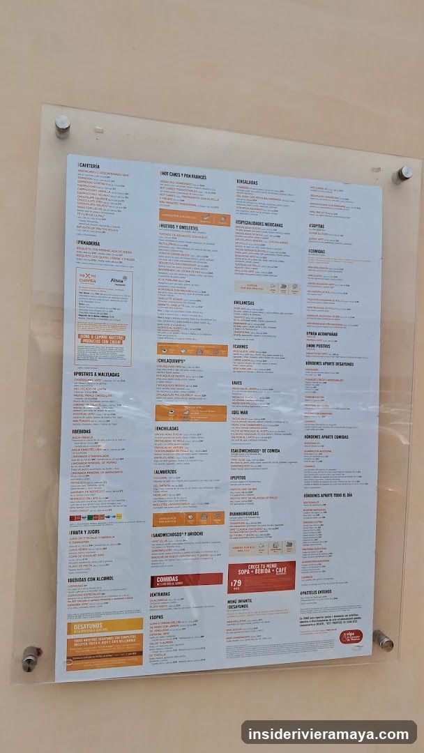 A large, laminated menu board mounted on a beige wall with clear acrylic holders. The menu is organized into multiple columns with categories such as Cafeteria, Panadería, Postres y Omelettes, Desayunos, and Combos. There are orange and red accent boxes highlighting specific deals like 'Menú del Día' and 'Sopa + Ensalada + Café'.