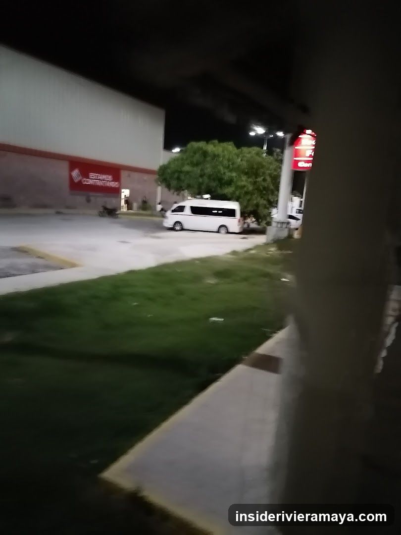 A nighttime view of a commercial building exterior. A large white van is parked in the lot. The building has a red sign with white text that reads 'ESTIMATED CONTRACTORS'. There is a grassy area in the foreground and a sidewalk.