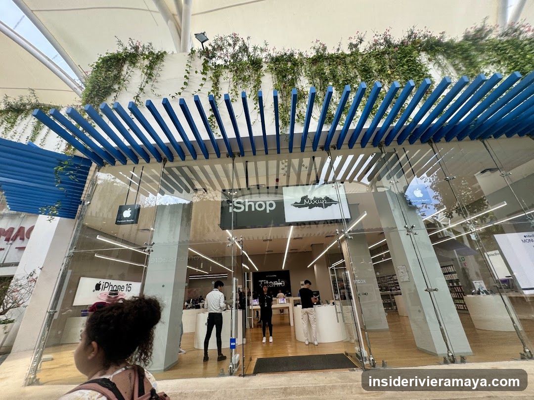 A view of a modern retail store entrance featuring a distinctive blue slatted pergola roof and hanging greenery. The storefront has glass walls and doors, with signage reading 'Shop' and 'Monsieur' visible above the entrance. Inside, customers and staff are visible near white display counters, and a sign for 'iPhone 15' is seen on the left.