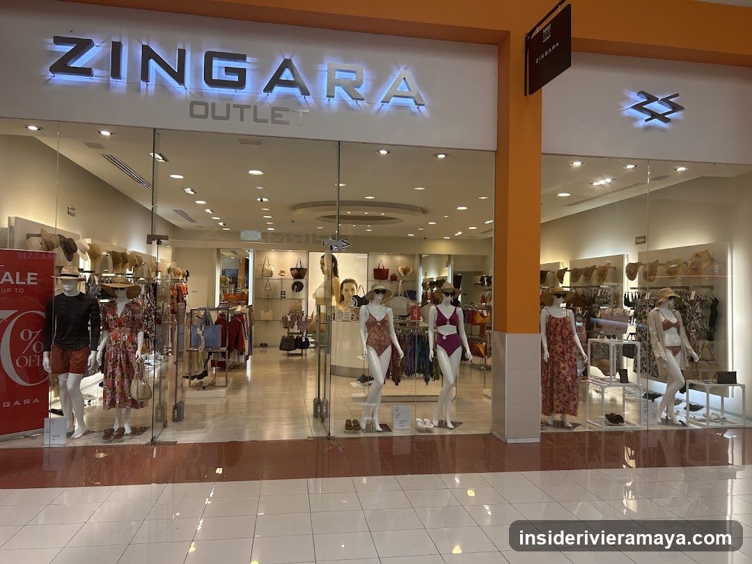 A brightly lit storefront for a store named 'ZINGARA OUTLET'. The name is displayed in large, illuminated letters above the entrance. The store features large glass windows and doors, displaying mannequins dressed in swimwear and summer clothing. A red sale sign is visible on the left side of the window display.