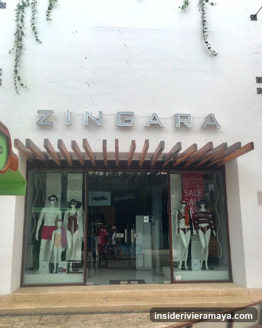 A white building facade features the store name 'ZINGARA' in large silver letters above the entrance. A wooden pergola structure extends over the glass storefront, which displays mannequins wearing swimwear and clothing. A red sale sign is visible in the right window.